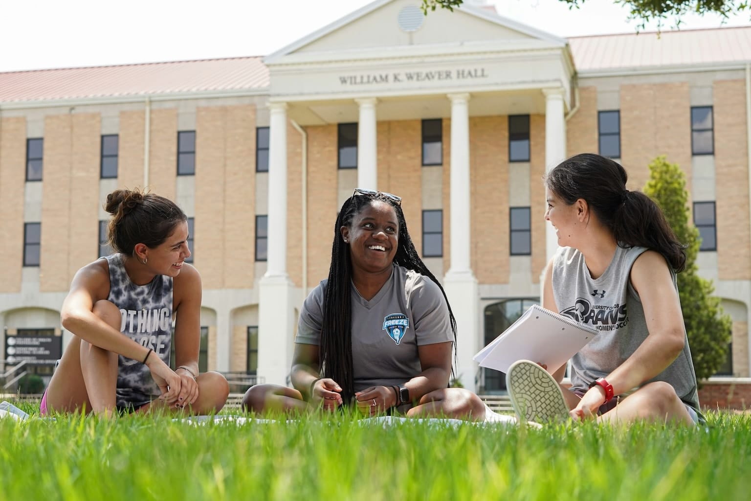 College students sitting on the grass, having a conversation about their classes.